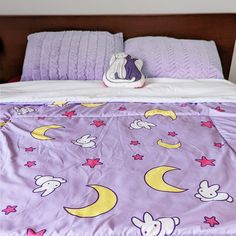 a bed with purple comforter and pillows on top of it, next to a stuffed animal