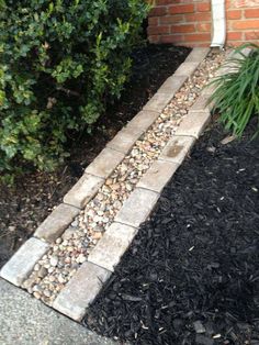 there is a brick walkway in front of the bushes and plants on the side of the house