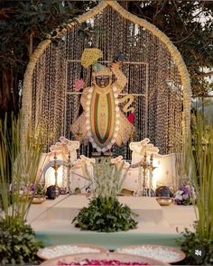 an idol is displayed in front of some plants and flowers on the table with other decorations