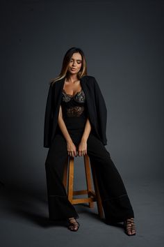 a woman sitting on top of a stool wearing black pants and a lace bralet