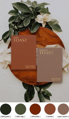 two brown books sitting on top of a wooden table next to green leaves and flowers