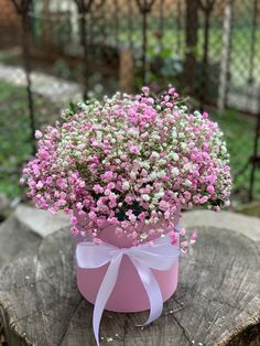 small pink and white flowers in a pink box on a tree stump with a bow