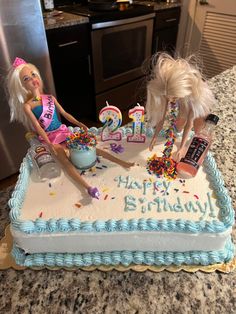 two barbie dolls are sitting on top of a birthday cake with candles and confetti