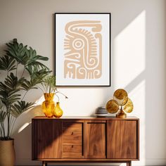 an art print hangs on the wall next to a wooden cabinet and potted plant