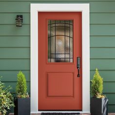 the front door is painted red and has two planters with plants in them next to it