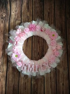 a wreath with pink flowers and the word mimi on it is hanging on a wooden wall