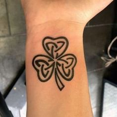 a black and white tattoo on the wrist of a person with a clover shaped design