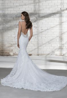 a woman in a white wedding dress standing against a brick wall with her back to the camera