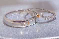 two wedding rings sitting on top of a silver surface with stars and moon decorations in the middle