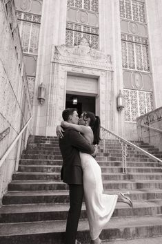 a man and woman hugging each other in front of a building with steps leading up to it