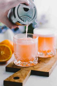 someone pouring orange juice into a glass on a cutting board with slices of an orange