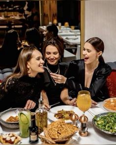 three women sitting at a table with food and drinks