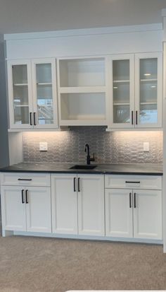 an empty kitchen with white cabinets and black counter tops on carpeted flooring in front of a gray wall