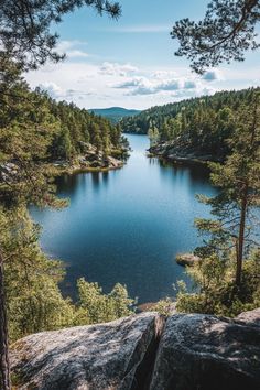 a lake surrounded by trees and rocks in the middle of a forest with blue sky