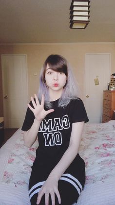 a woman sitting on top of a bed with her hand up in the air and wearing a t - shirt that says game on