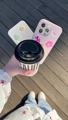 a person holding a coffee cup in their hand and an iphone case with stickers on it