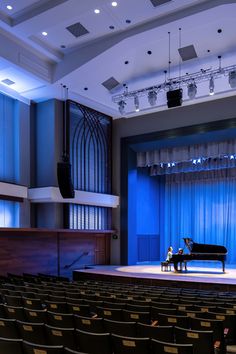 an empty stage with a piano and two people sitting at the table in front of it