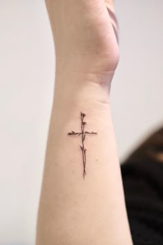 a small cross tattoo on the left side of the arm is shown in black ink