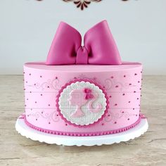 a pink cake decorated with a bow and monogram on it's top is sitting on a table