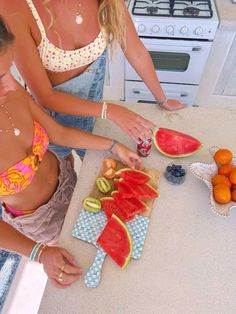 two women are cutting up watermelon slices on a counter top in the kitchen