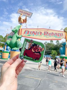 someone holding up a sticker in front of the entrance to an amusement park