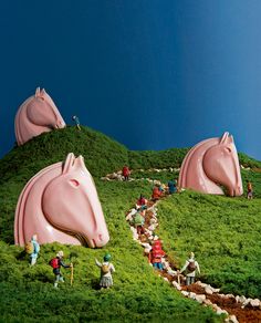 people are standing on the side of a grassy hill with pink horse heads in the grass