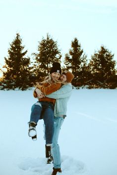 two people are hugging in the snow with trees in the background and one person is wearing boots