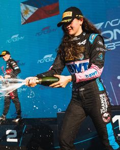 a woman is spraying champagne on her car while another man watches from the sidelines