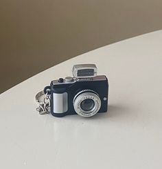 a camera keychain sitting on top of a white table next to a wall