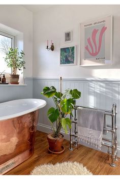 a bathroom with a copper bathtub, plant and pictures on the wall above it