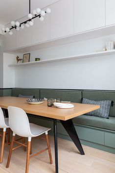 a dining table with white chairs and plates on it in front of a bench that is built into the wall