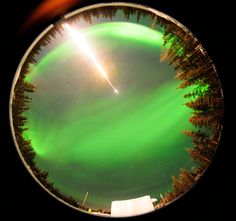 an image of the northern lights through a magnifier lens with trees in the foreground