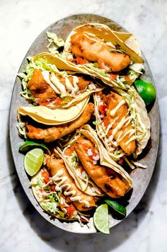 a plate filled with tacos and shrimp on top of a table next to limes