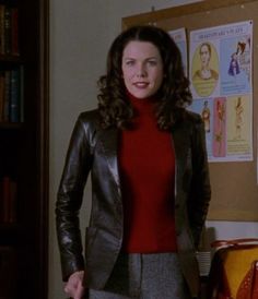 a woman standing in front of a bookshelf wearing a red sweater and black leather jacket