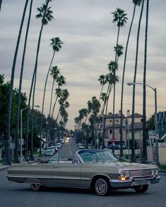 an old car is parked on the side of the road in front of palm trees