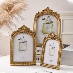 three ornate gold frames sitting on top of a white table next to a vase with flowers