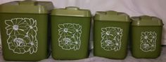 four green canisters with flower designs on them sitting next to each other in front of a white curtain