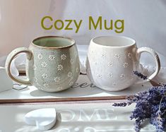 two mugs sitting next to each other on top of a white tray with purple flowers