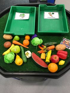 two trays filled with different types of fruits and vegetables sitting on top of a grass covered table