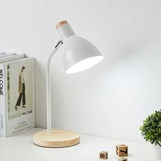 a white desk lamp sitting on top of a table next to a book and plant