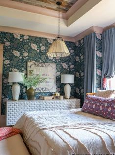 a bedroom with blue floral wallpaper and white bedding, two lamps on either side of the bed