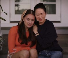 two women sitting on the ground next to each other and one is touching her hair