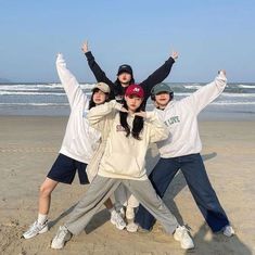 four people standing on the beach with their arms in the air