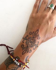 a woman's hand with tattoos and bracelets on her wrist, next to a white wall