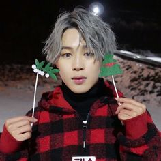 a person holding up two stick with leaves on top of their heads and wearing a plaid jacket