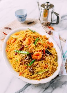 a white bowl filled with noodles and shrimp on top of a marble countertop next to silverware