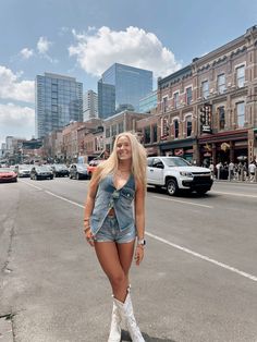 a woman standing in the middle of an empty street with tall buildings and cars behind her