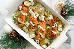 a white dish filled with potatoes and salmon on top of a marble table next to pine cones