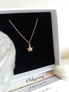 a gold necklace with a star on it sitting in front of a black box next to a white rock