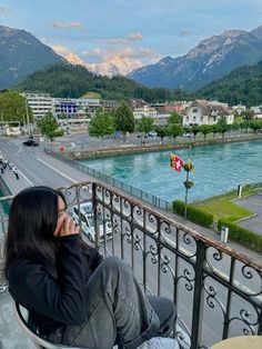 a woman sitting on top of a balcony talking on a cell phone next to a river